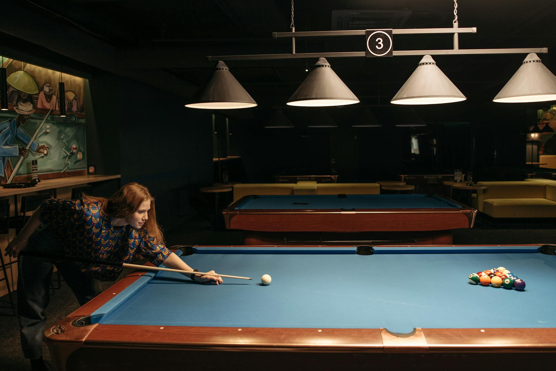 Kobieta celująca kijem bilardowym przy stole w ciemnej sali