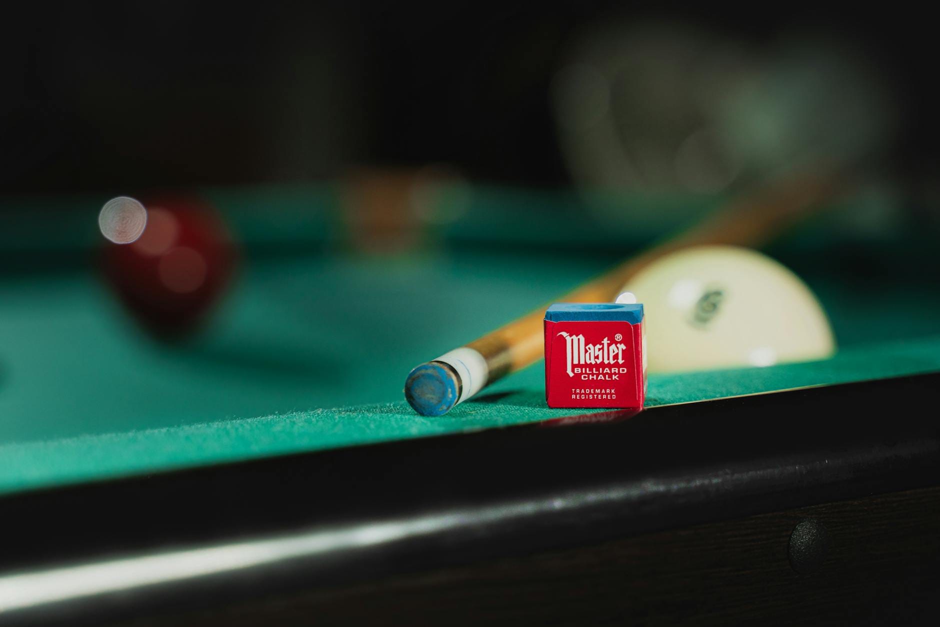 Kij bilardowy, kreda i biała bila leżące na zielonym stole bilardowym