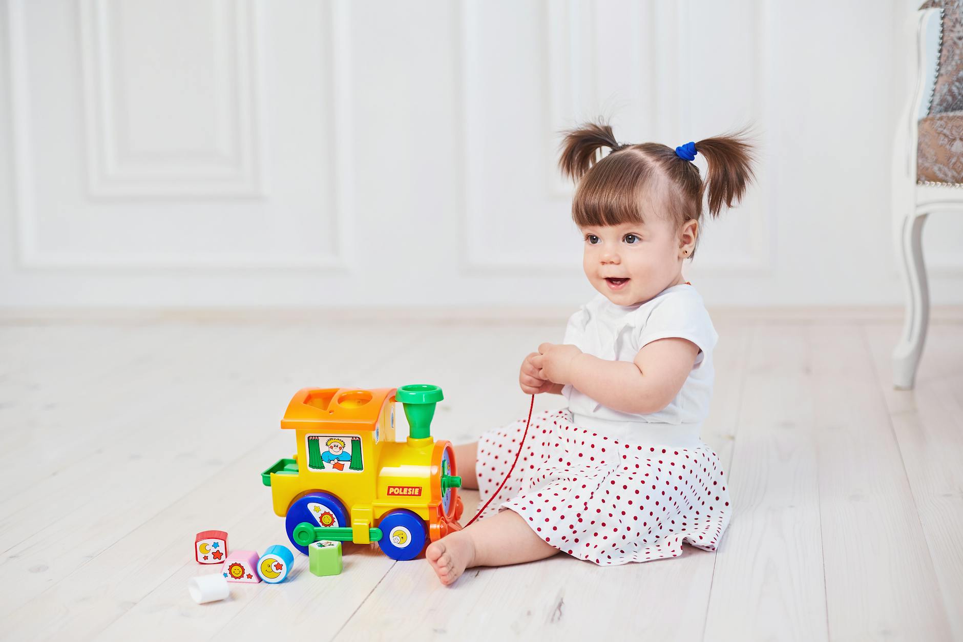 Dziewczynka bawi się kolorowym pociągiem na drewnianej podłodze