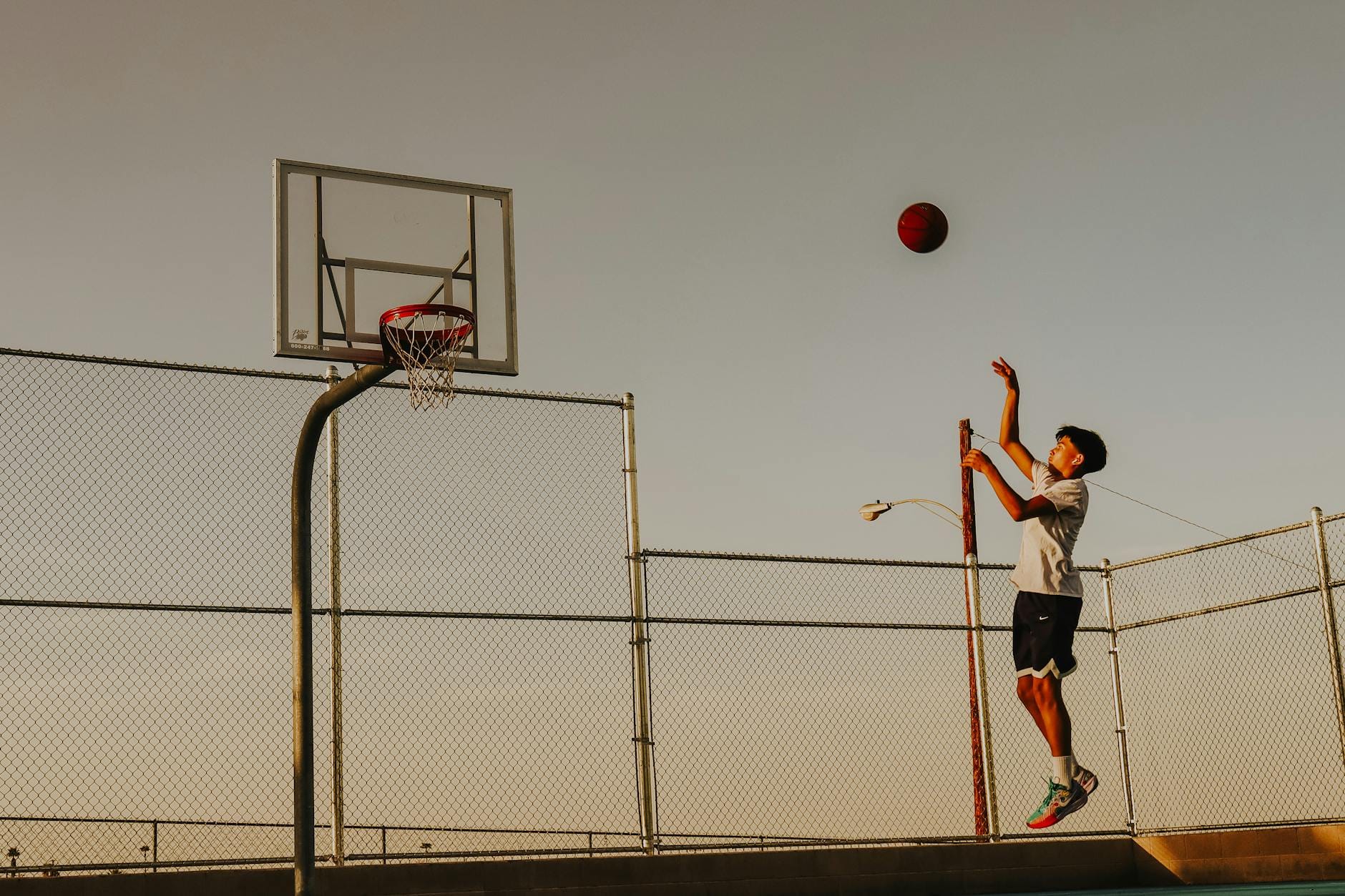 Nastolatek trenuje rzuty do kosza na boisku o zachodzie słońca