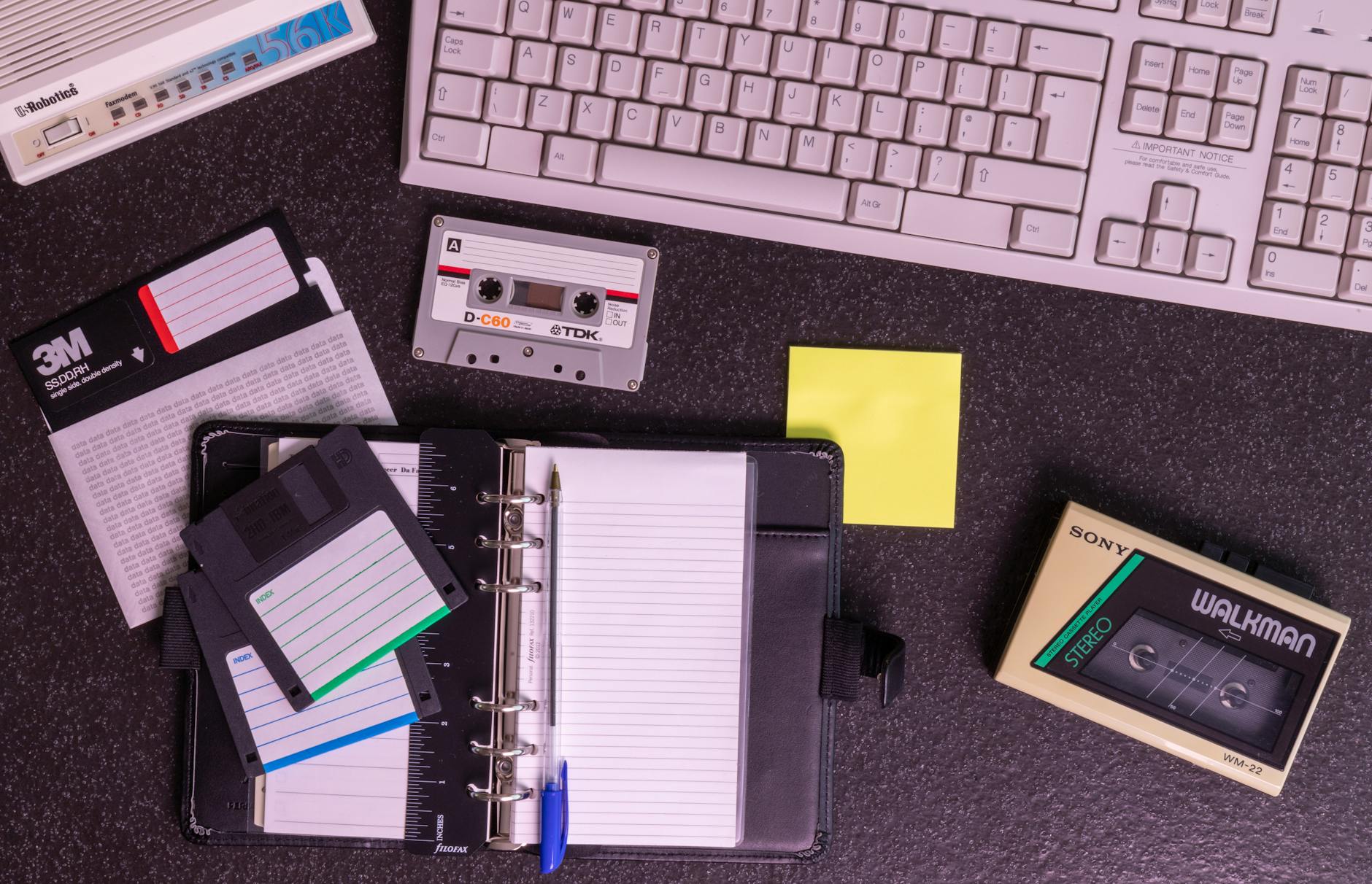 Retro sprzęt elektroniczny na biurku: walkman, dyskietki i klawiatura