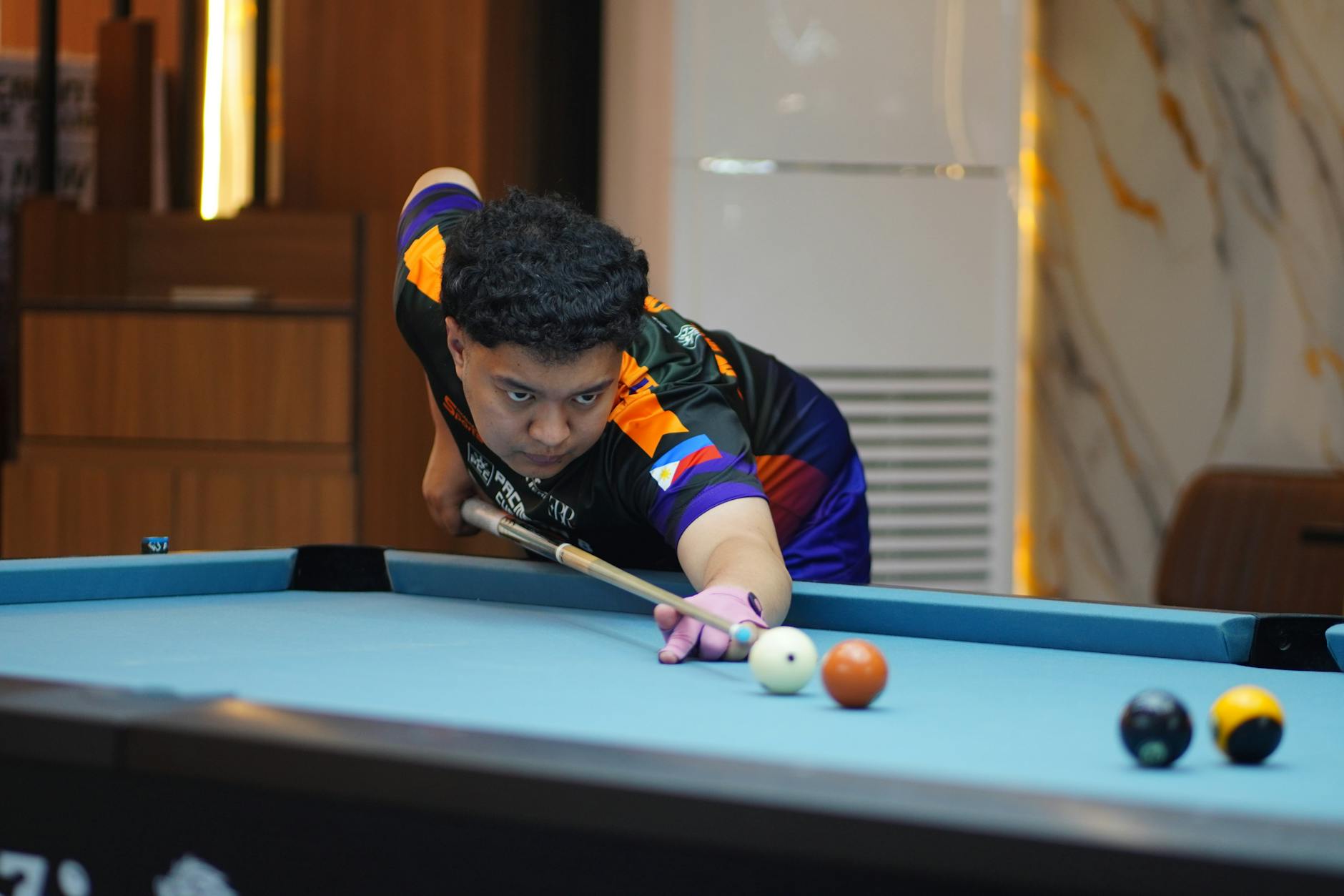 Młody gracz bilardowy celuje kijem w białą bilę przy trudnym układzie