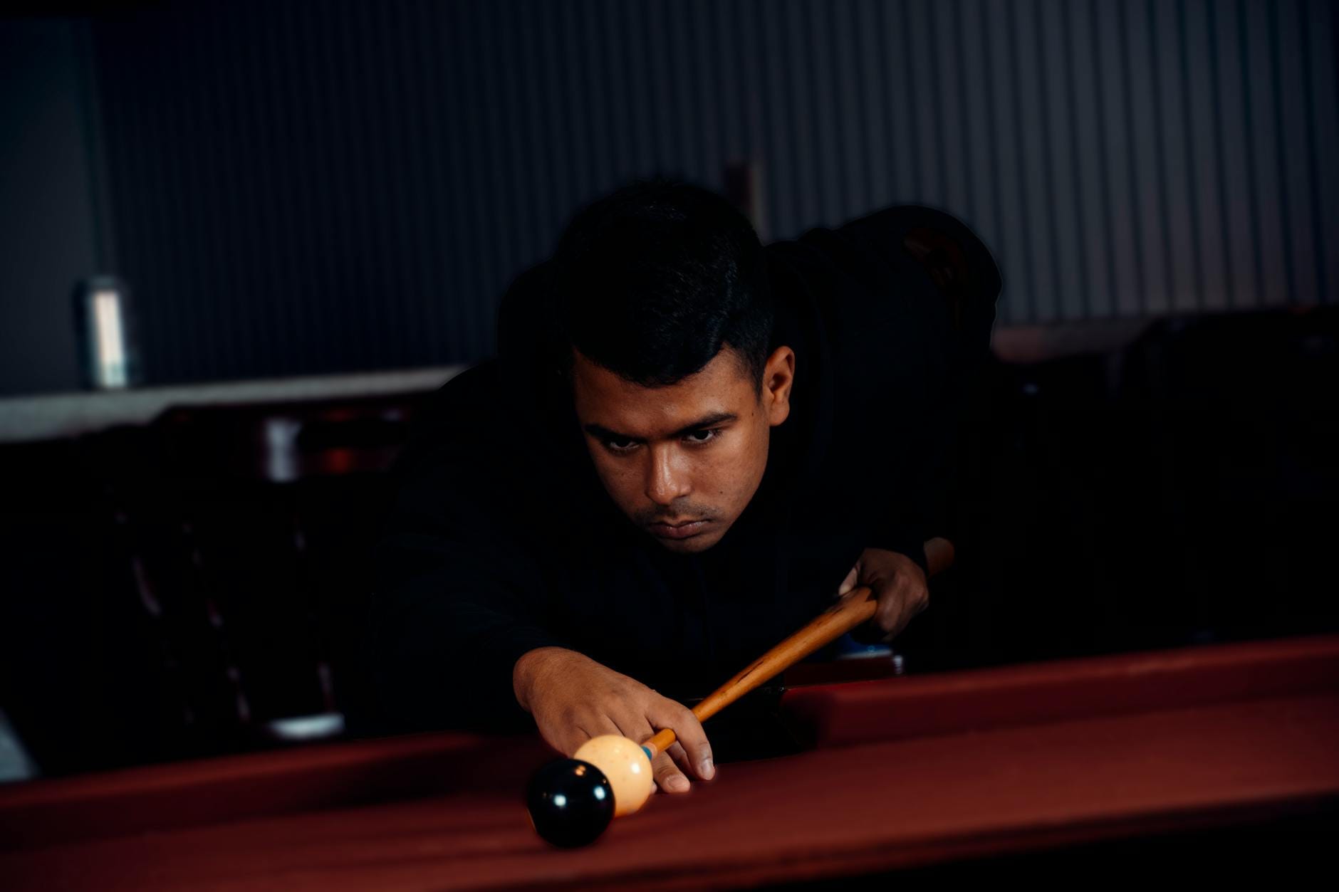 Skupiony mężczyzna celuje kijem bilardowym podczas gry w bilard